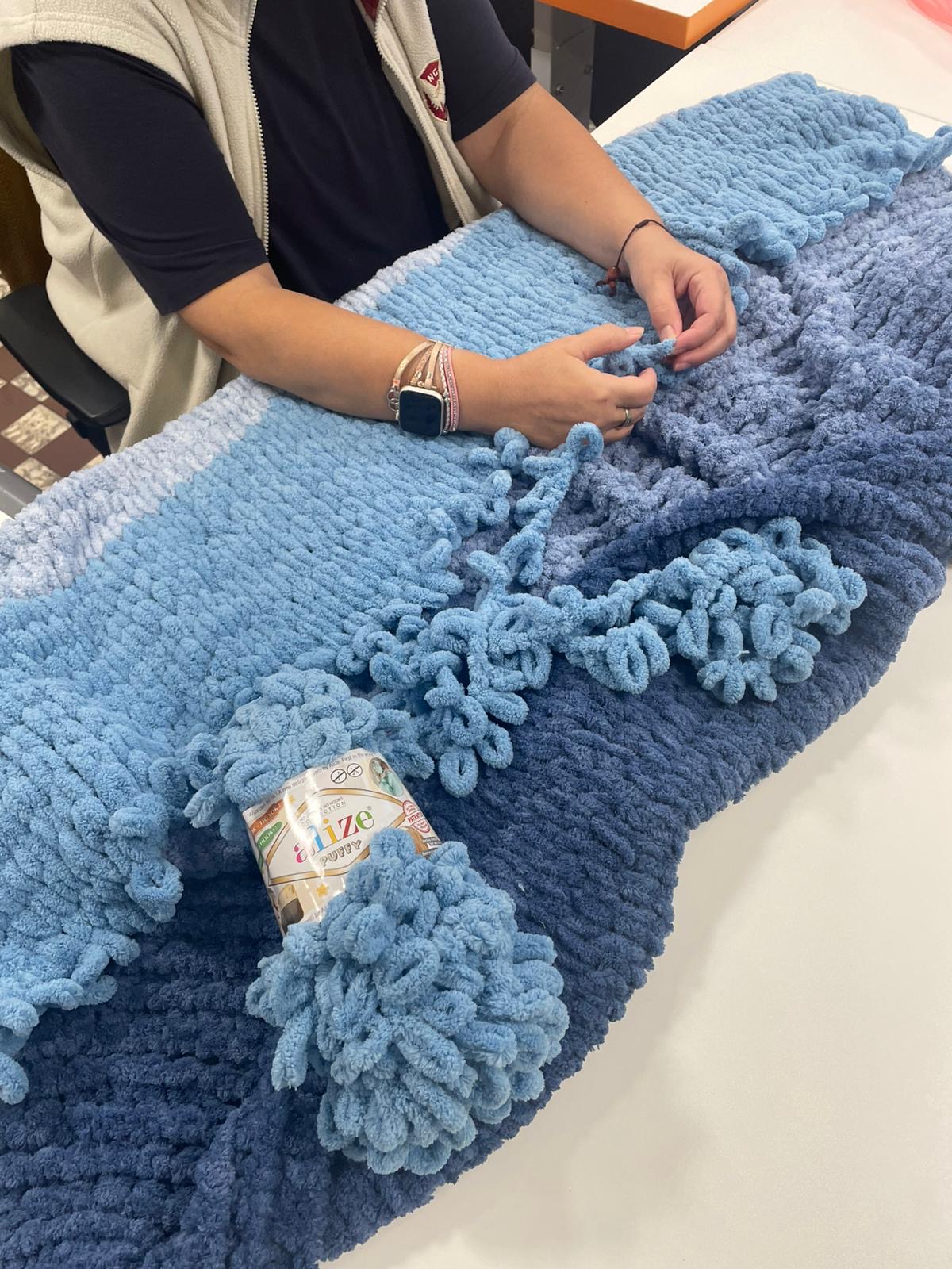 Ruce pracující s měkkou modrou dekou z příze